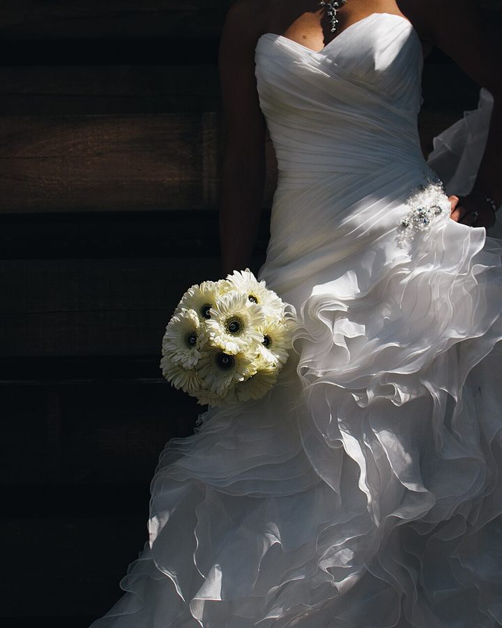 Bride in a ruffled white gown holding a bouquet of white daisies