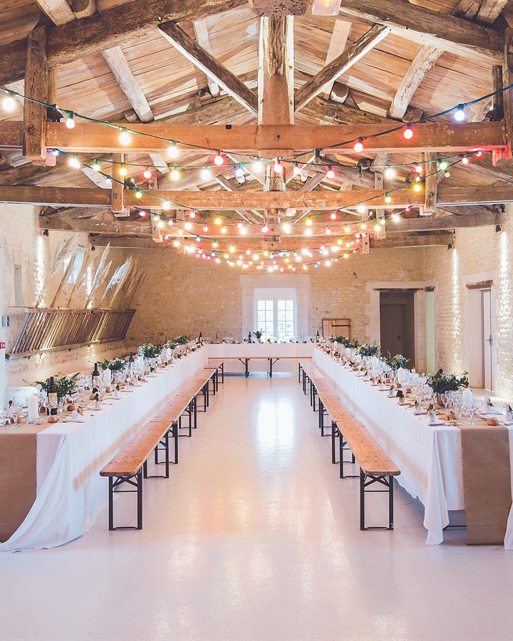 Long reception tables with string lights beneath rustic wooden beams