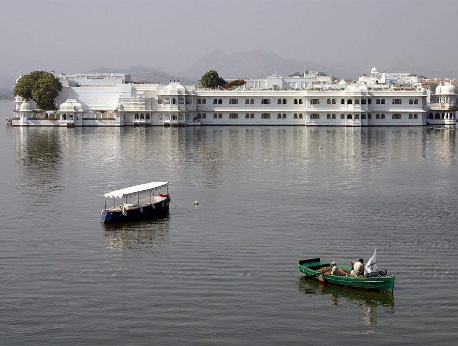 White palace rising from a calm lake with small boats in the foreground